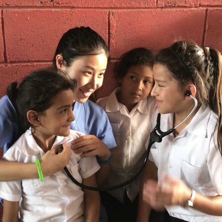 A GMMA healthcare worker sharing a stethoscope with schoolchildren in Honduras