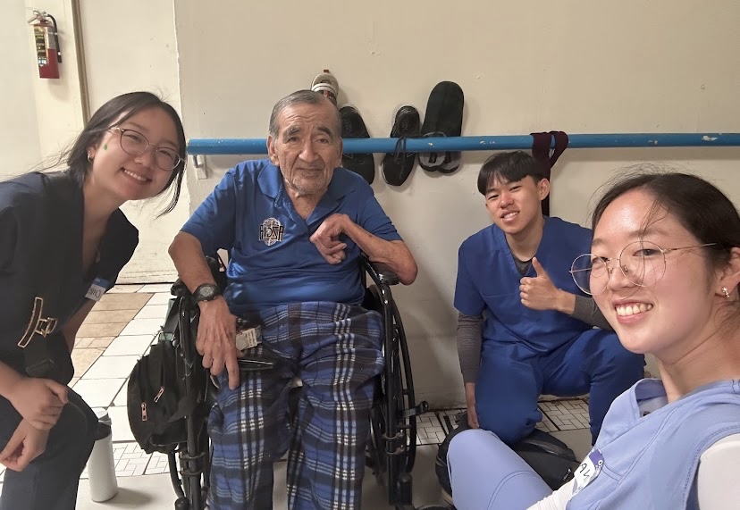 High school students smiling with an elderly man in a wheelchair during a visit