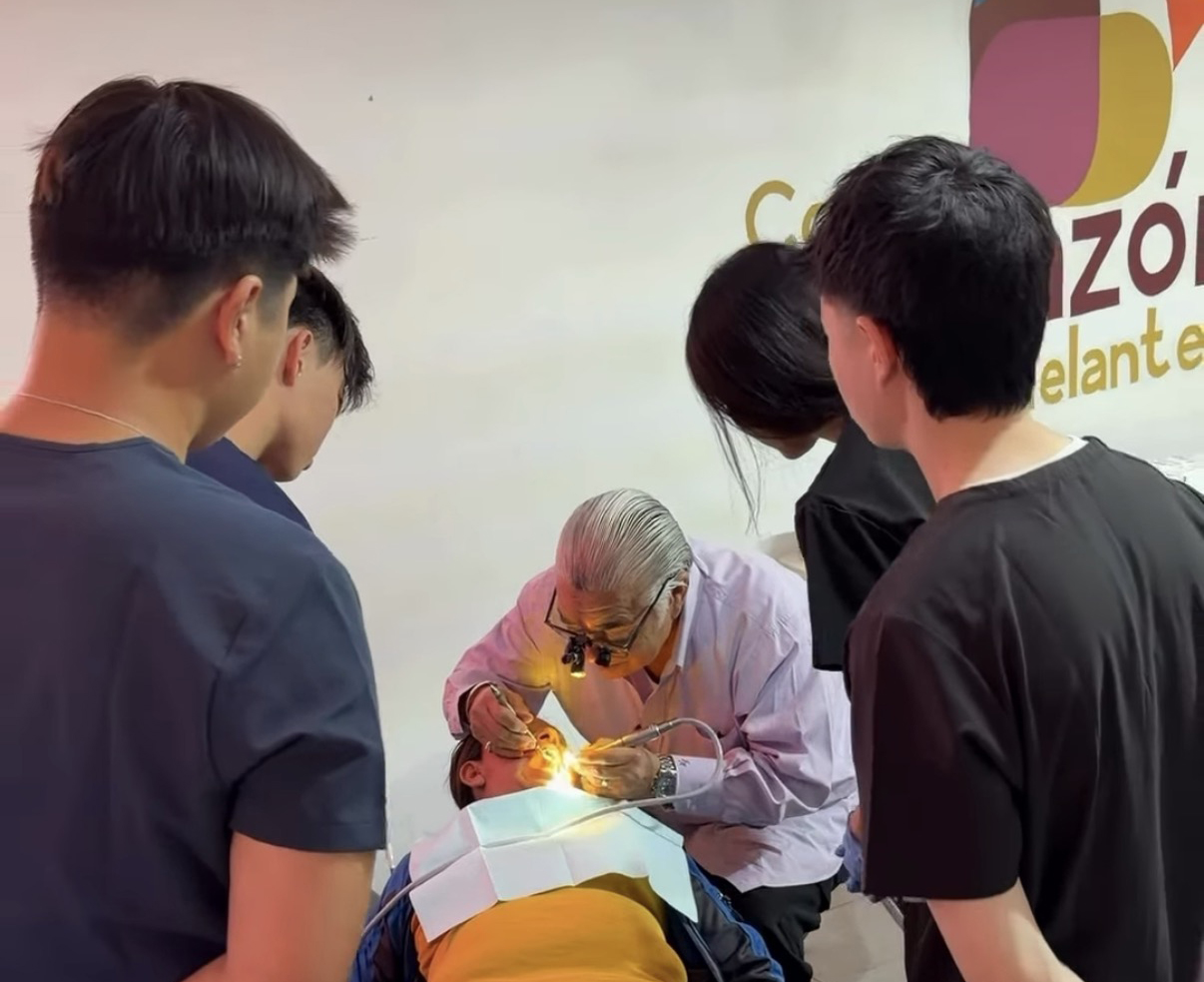 A dentist leading a hands-on dental exam for students observing closely during a mission clinic